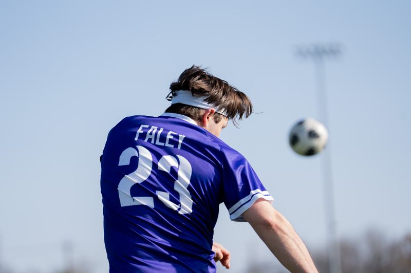 A player in purple heads the ball against a blue sky